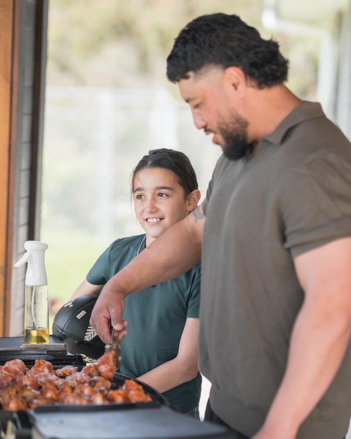 A father and daughter cooking together at a backyard grill